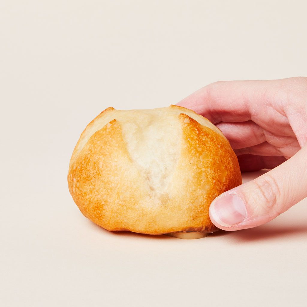 A hand touches a lamp that mimics the size, shape and texture of a baked dinner roll