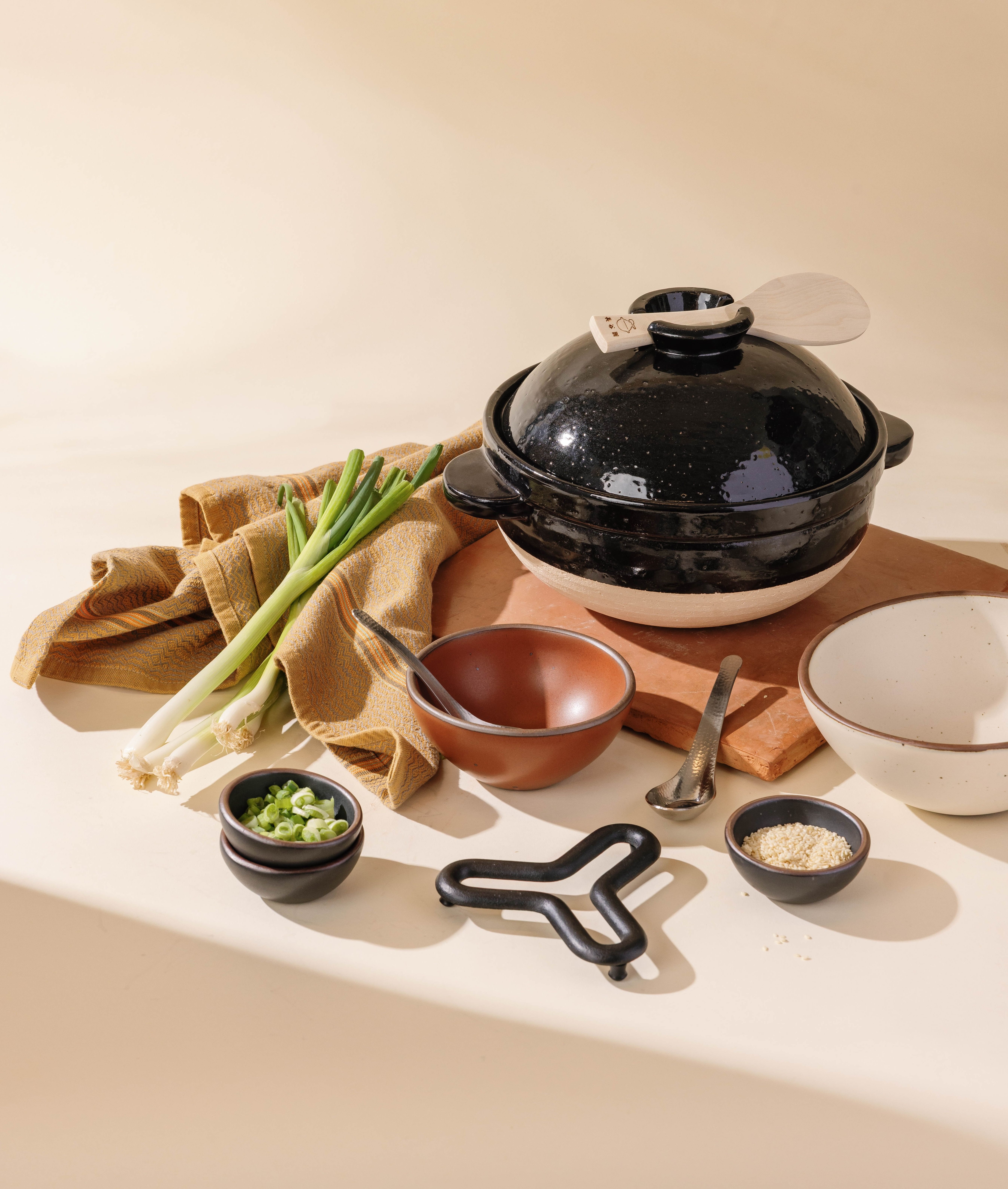 An overhead view of people partaking in a feast with kebabs on a cast iron plate, a donabe with rice, and other foods with white plates and dinner napkins.