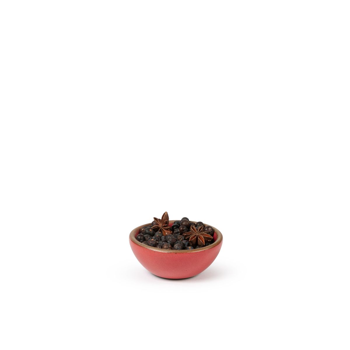 A tiny rounded ceramic bowl in a bold red color featuring iron speckles and an unglazed rim, filled with dried seasoning