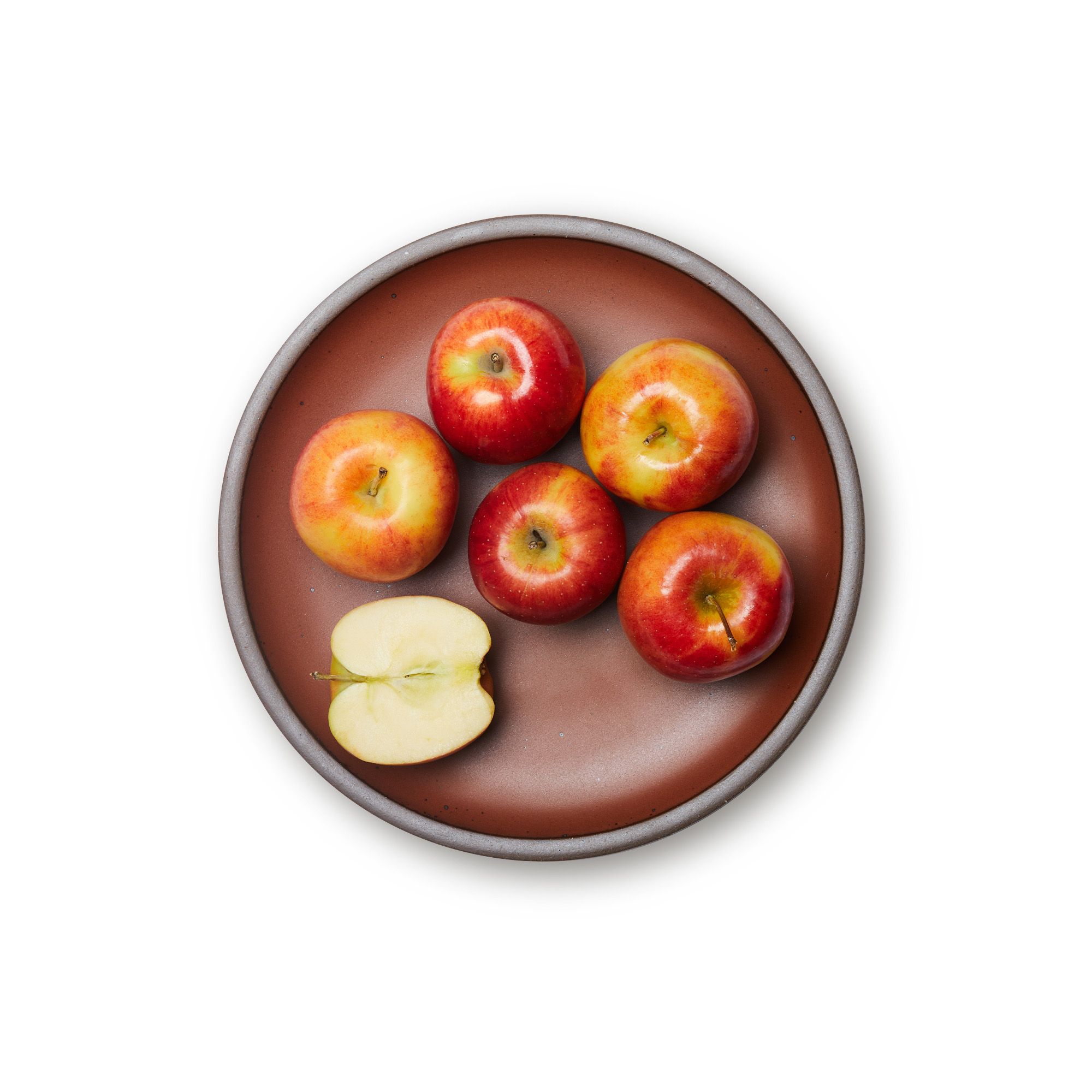 Apples on a dinner sized ceramic plate in a cool burnt terracotta color featuring iron speckles and an unglazed rim.