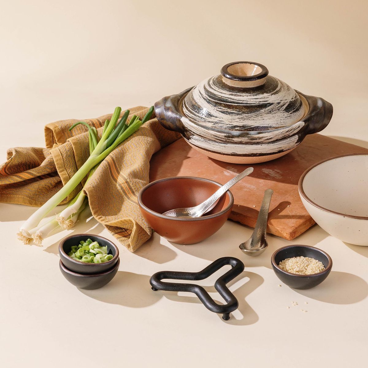 Donabe with bold black-and-white brushwork, styled with serving bowls, utensils, and fresh ingredients on a warm tabletop.