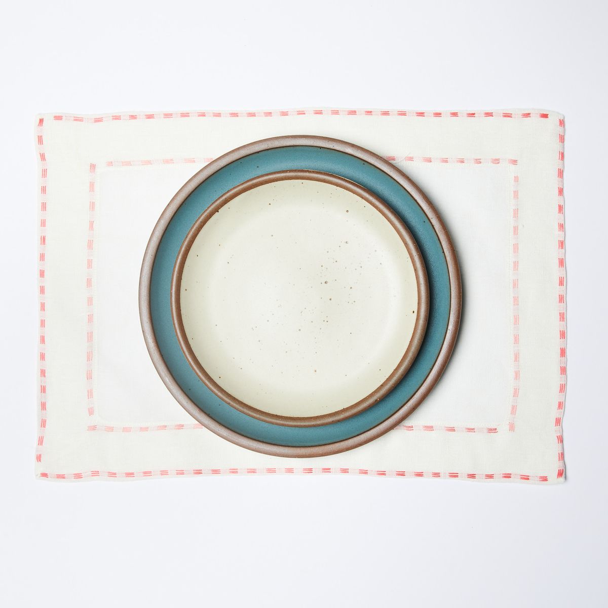 White placemat with coral border, blue and white stacked plates on top