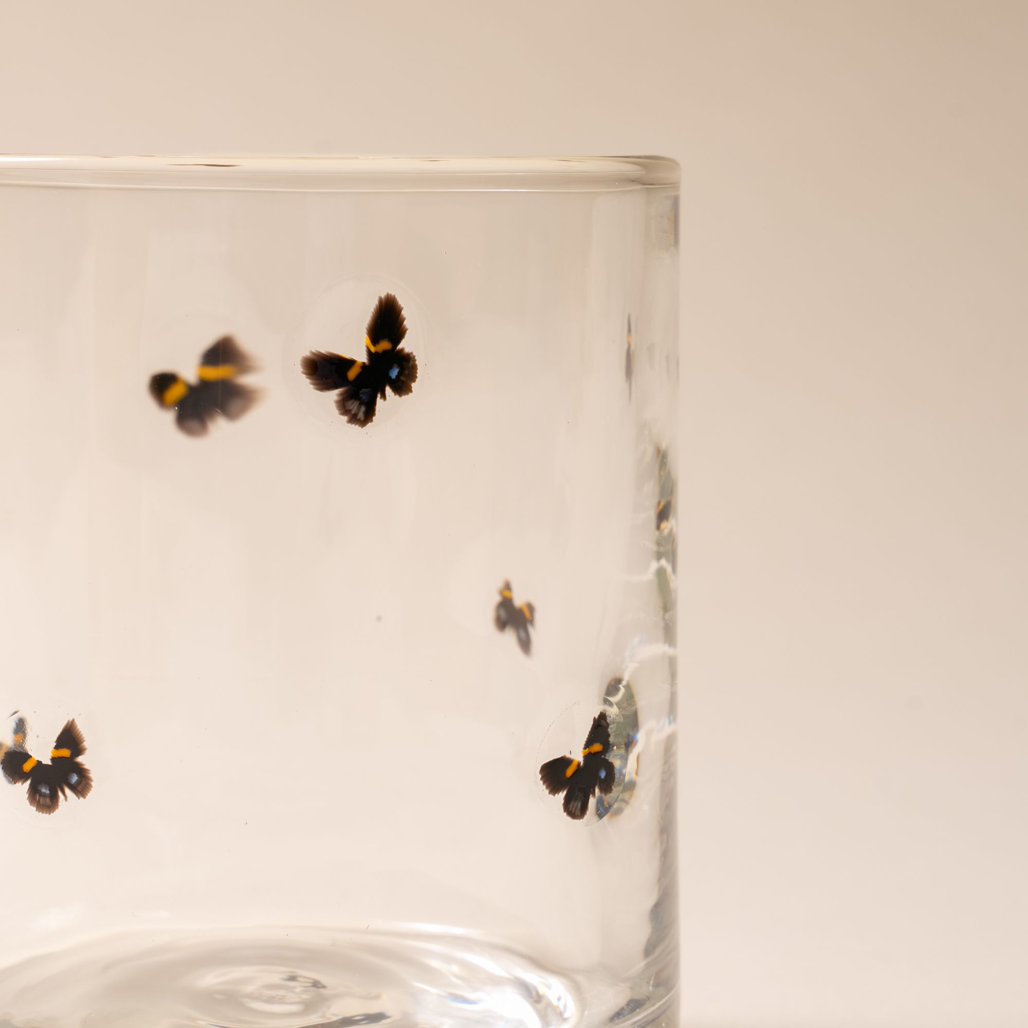 A close up of a clear glass with a ring of butterflies on a cream background.