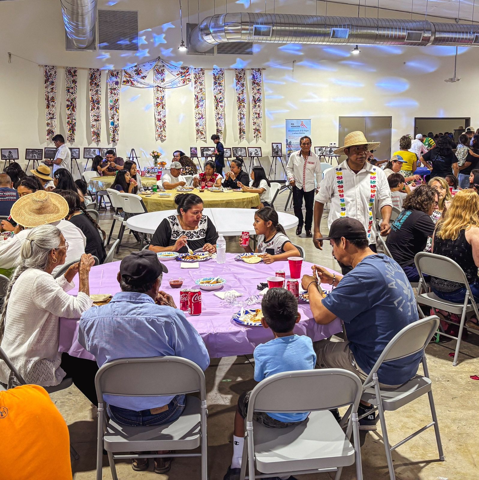 People sit at large round tables inside at a festive party in a large open space