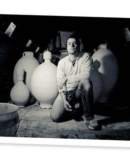 A black and white photo of Alex Matisse kneeling in front of large ceramic pieces in a wood kiln