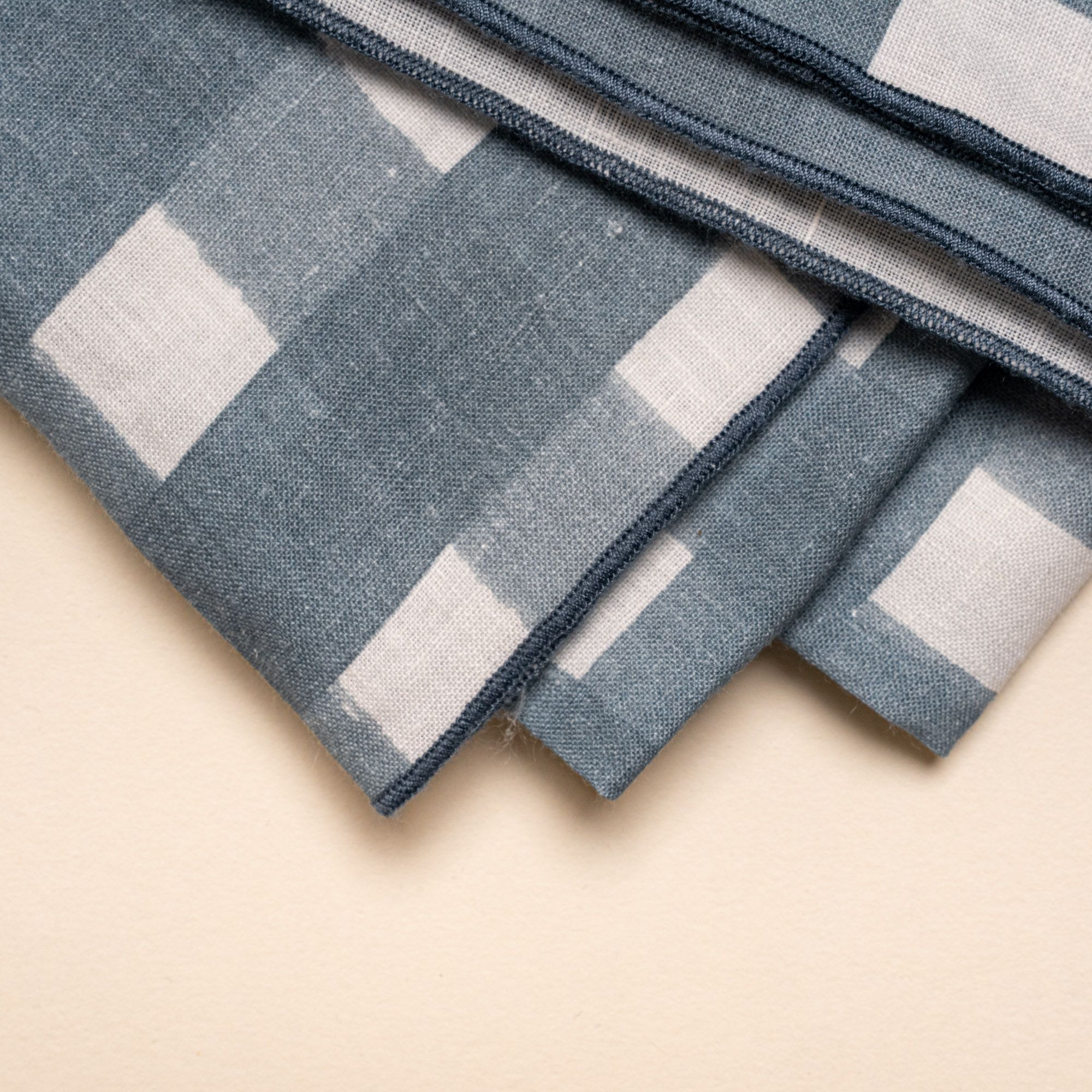 A closeup of a folded tablecloth featuring a blue-grey crosshatch pattern with navy edges.