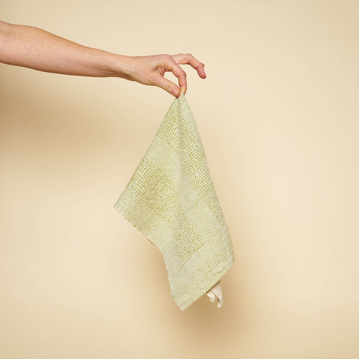 A finger holding up a green-and-natural woven tea towel