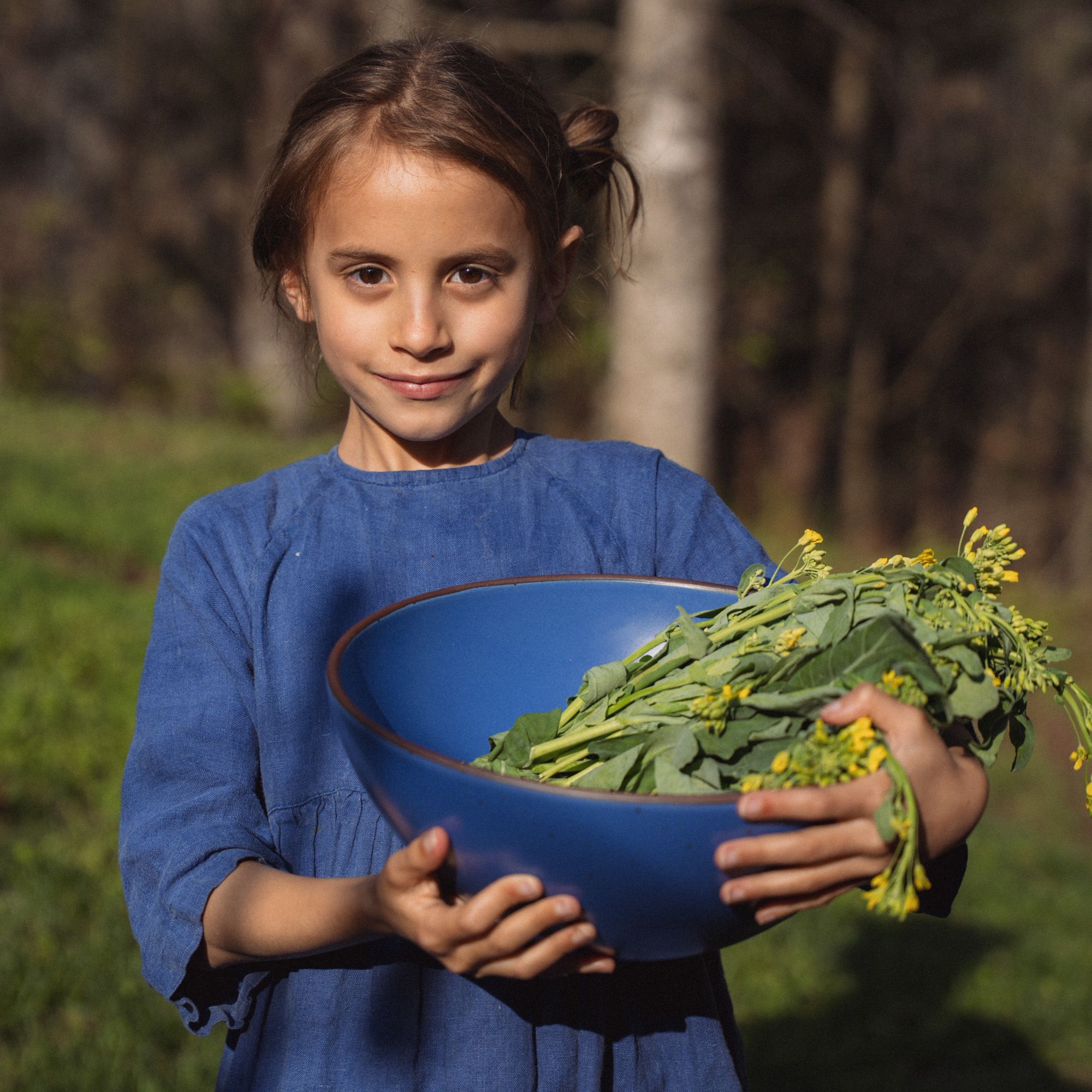Lucia is outside and holding a large ceramic mixing bowl in a cobalt blue color filled with greenery