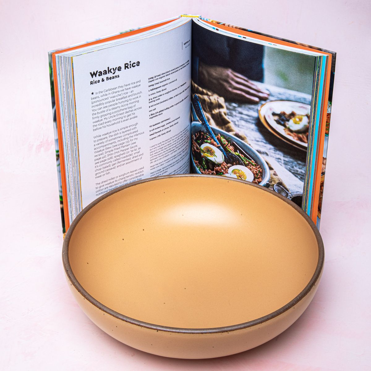 A large serving bowl in a peachy yellow color with an open book featuring a recipe and a close up look at a bowl of food