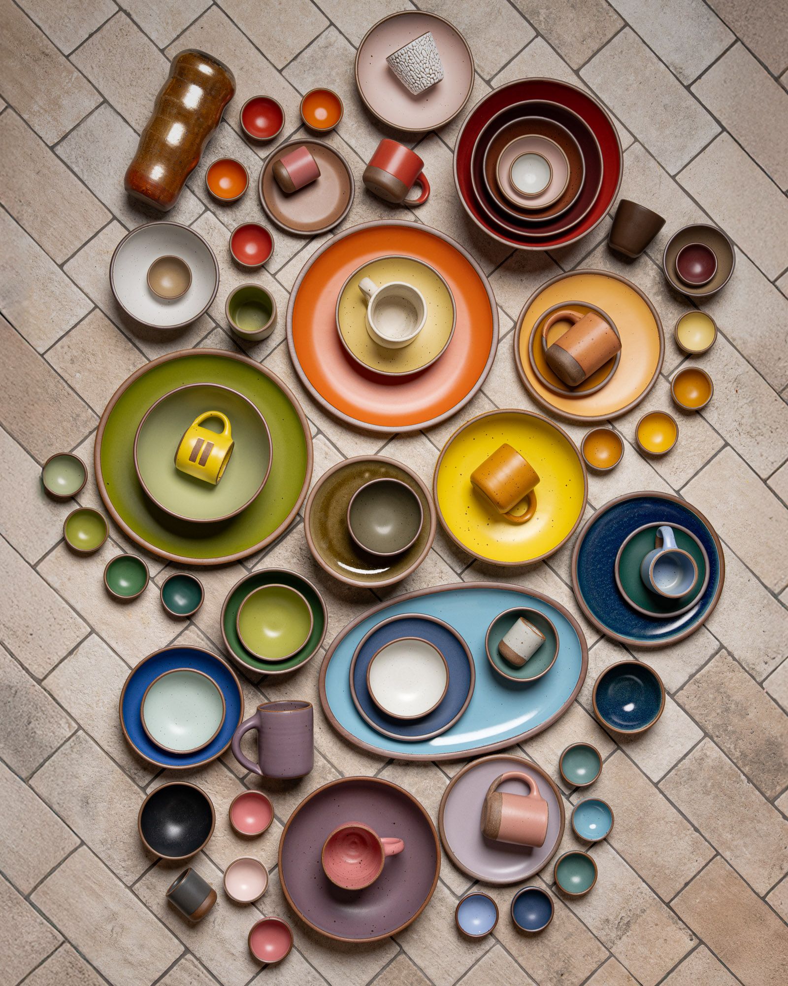 Ceramic dinnerware of plates, platters, bowls, mugs and cups are all artfully arranged close together all in different colors of the rainbow.