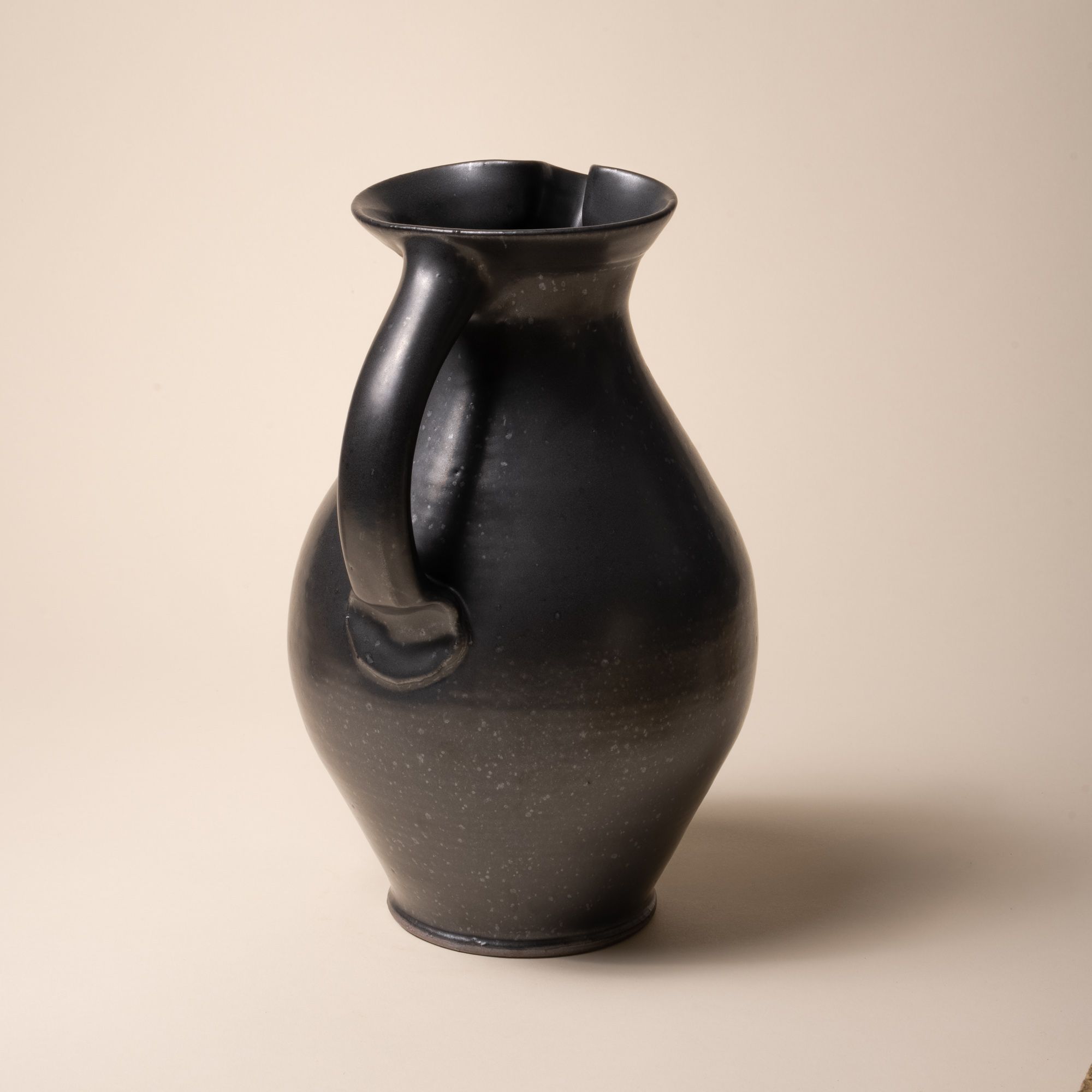 A hand-formed large classic ceramic pitcher with a spout and handle in a black graphite color with iron speckles