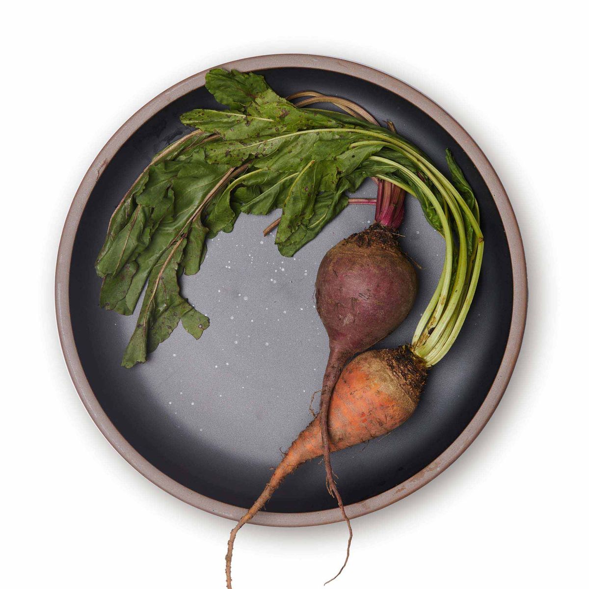 Root vegetables on a large ceramic platter in a graphite black color featuring iron speckles and an unglazed rim.
