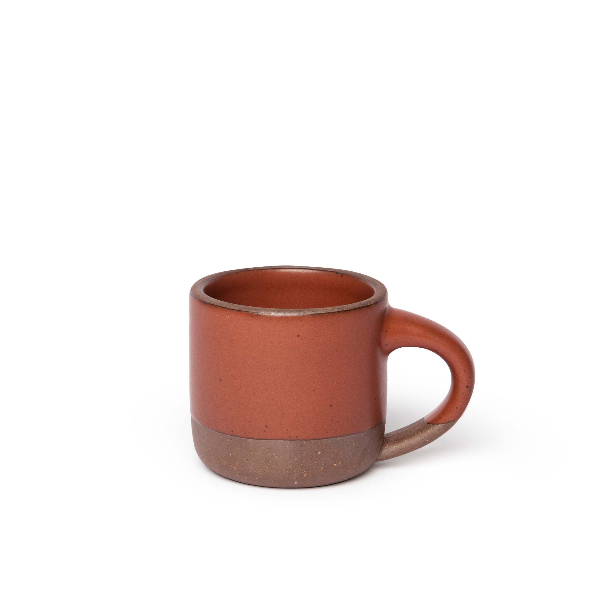A small sized ceramic mug with handle in a cool burnt terracotta glaze featuring iron speckles and unglazed rim and bottom base.