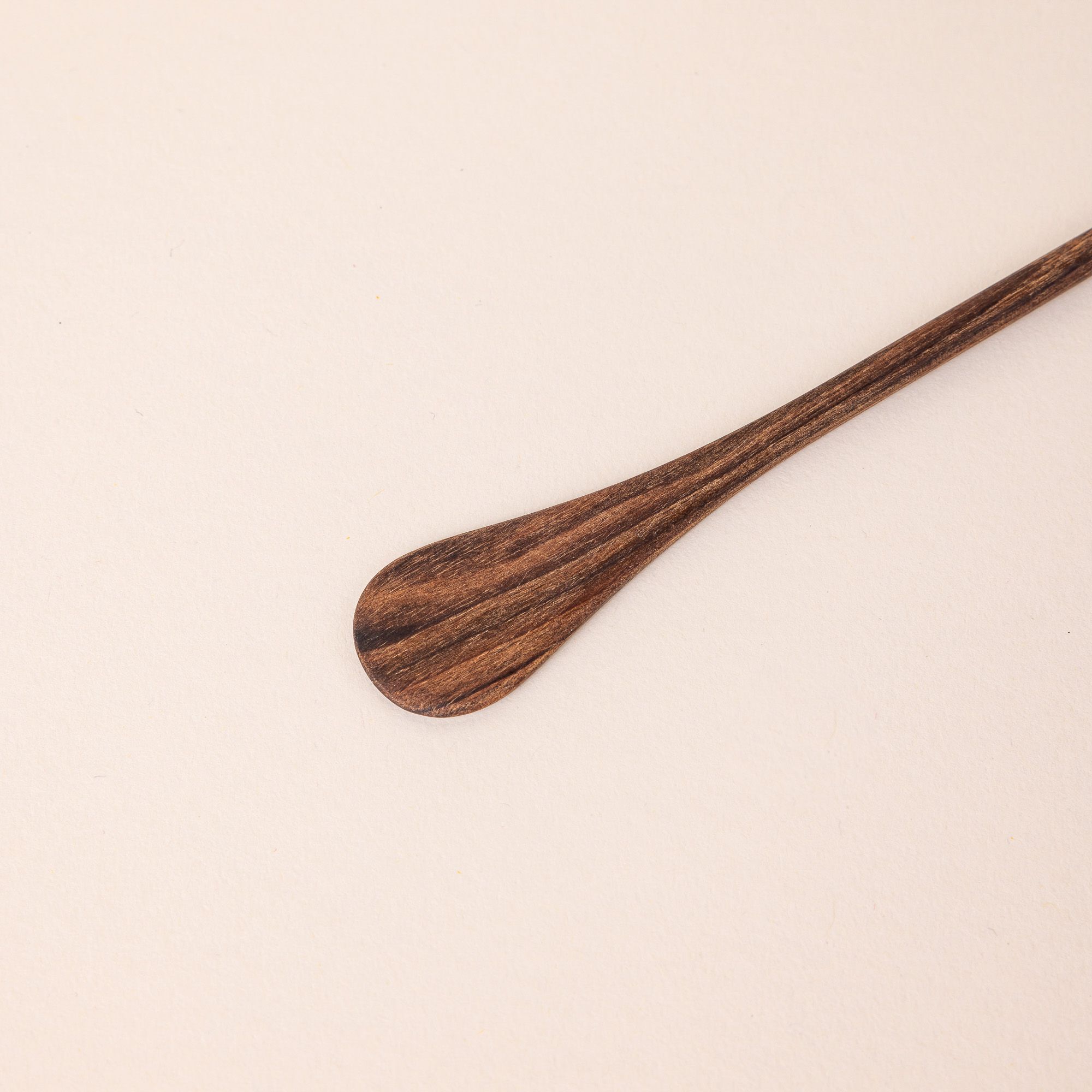 A close up of the end of a walnut cocktail stirrer. The end has a small spoon-like shape.