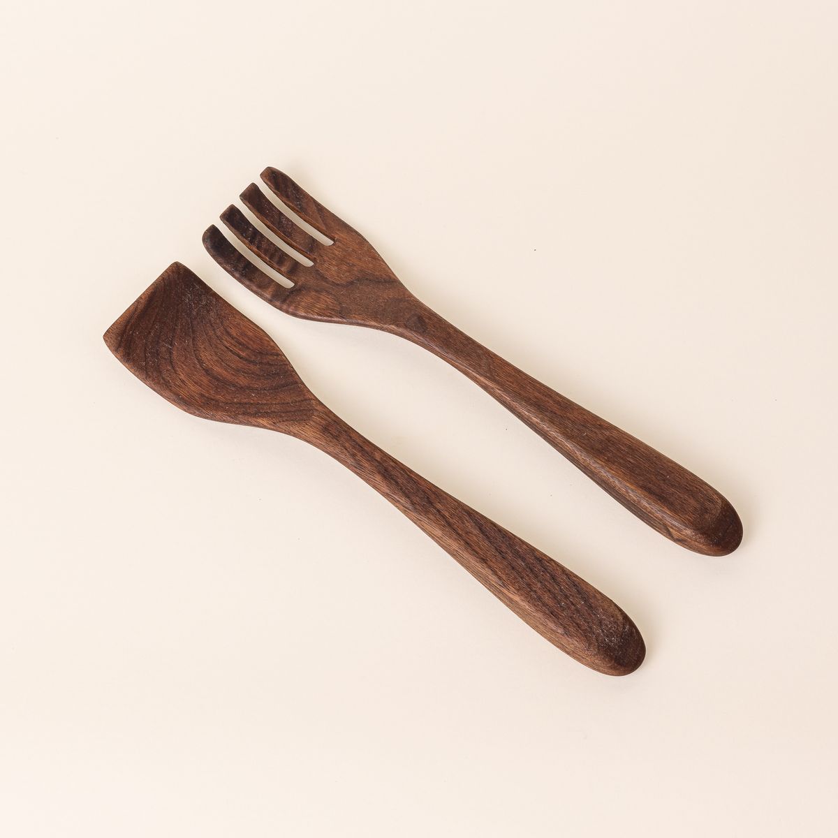 Two long walnut wood serving utensils. The left utensil has a shape like a spatula, the right has a shape like a fork.
