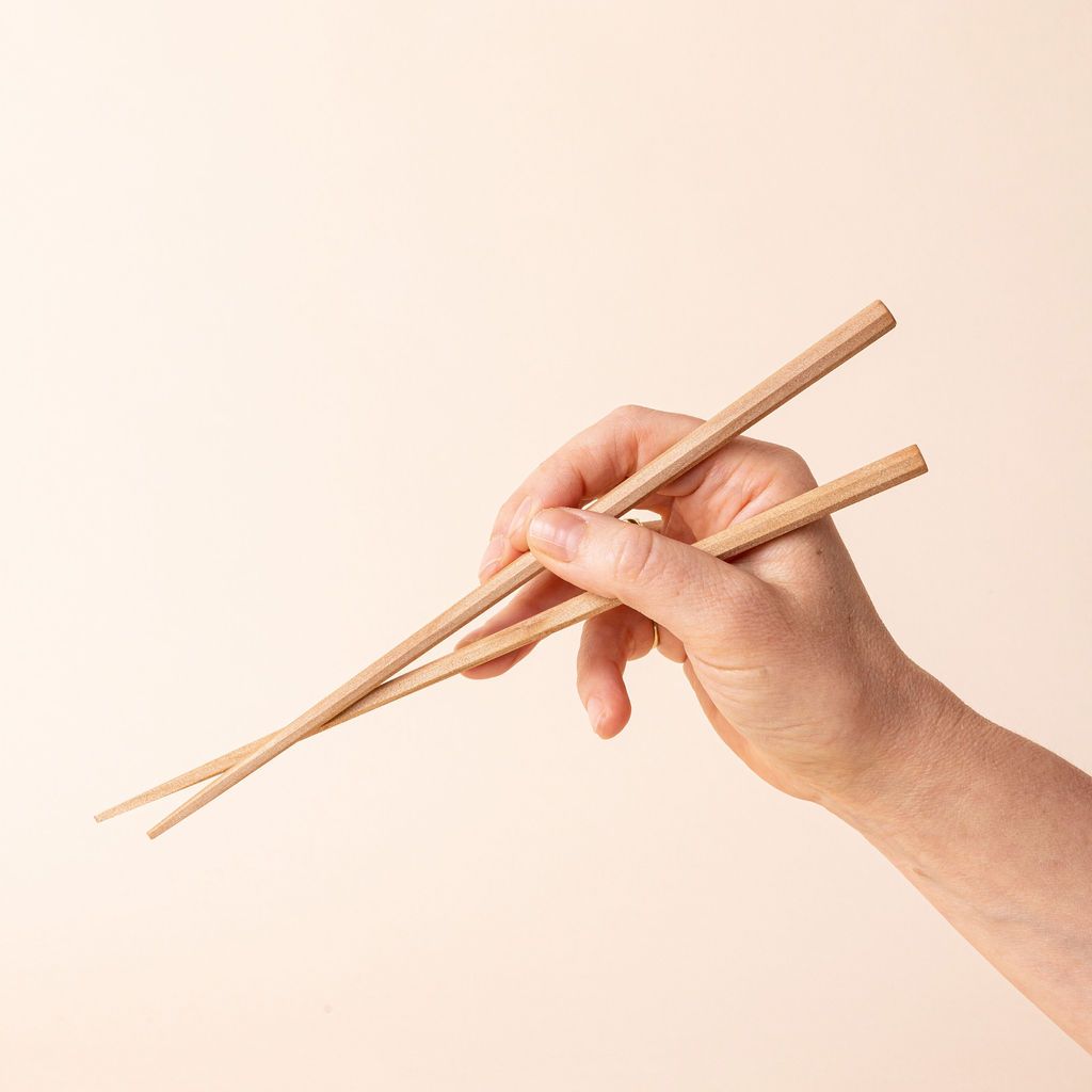 A hand holding simple light wood chopsticks