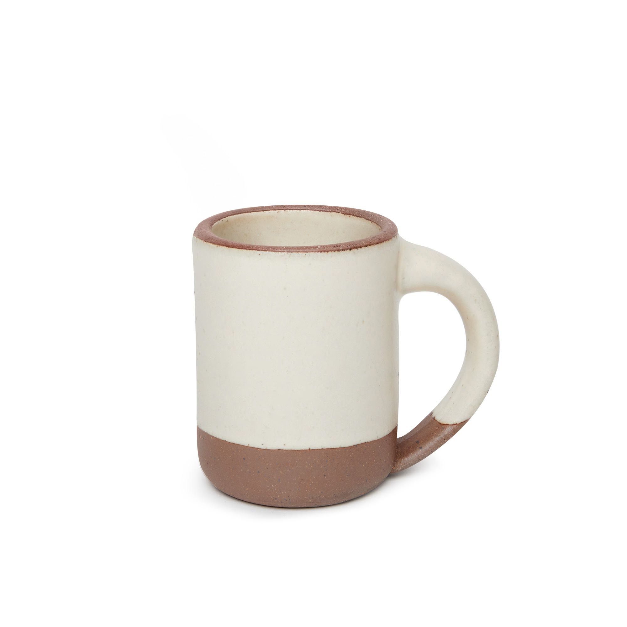 A medium sized ceramic mug with handle in a warm, tan-toned, off-white color featuring iron speckles and unglazed rim and bottom base.