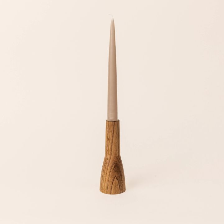 A butternut wood candle holder that is narrow shaped with a wider base on the bottom half and a thinner cylinder on the top half. A taper candle sits on the top. 