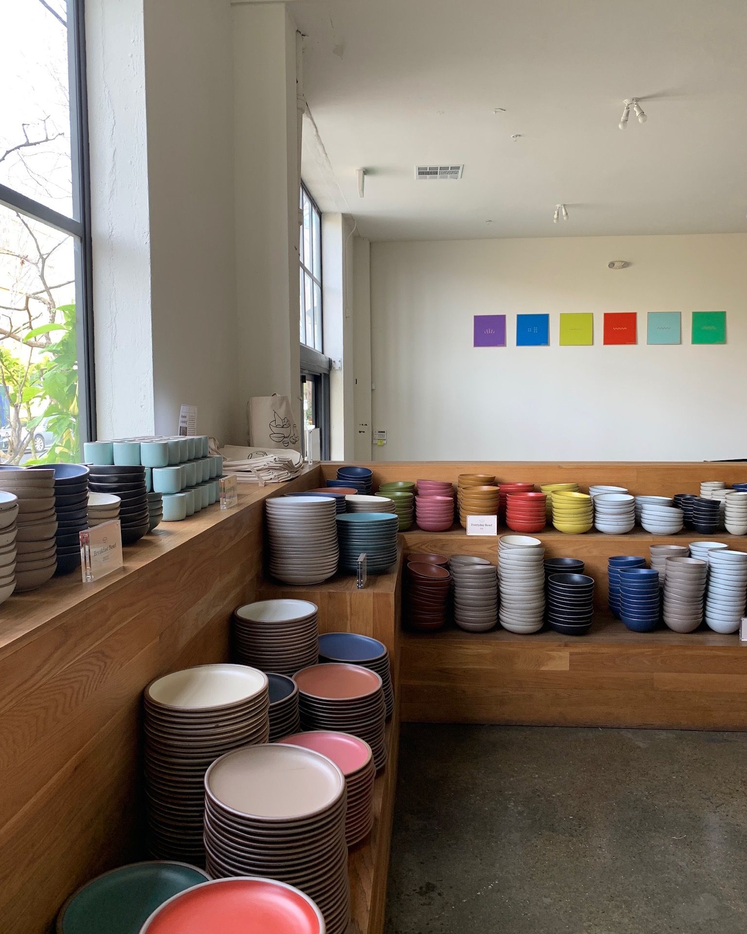 In a retail setting, there are large stacks of ceramic bowls and plates in all different colors of the rainbow arranged on shelves