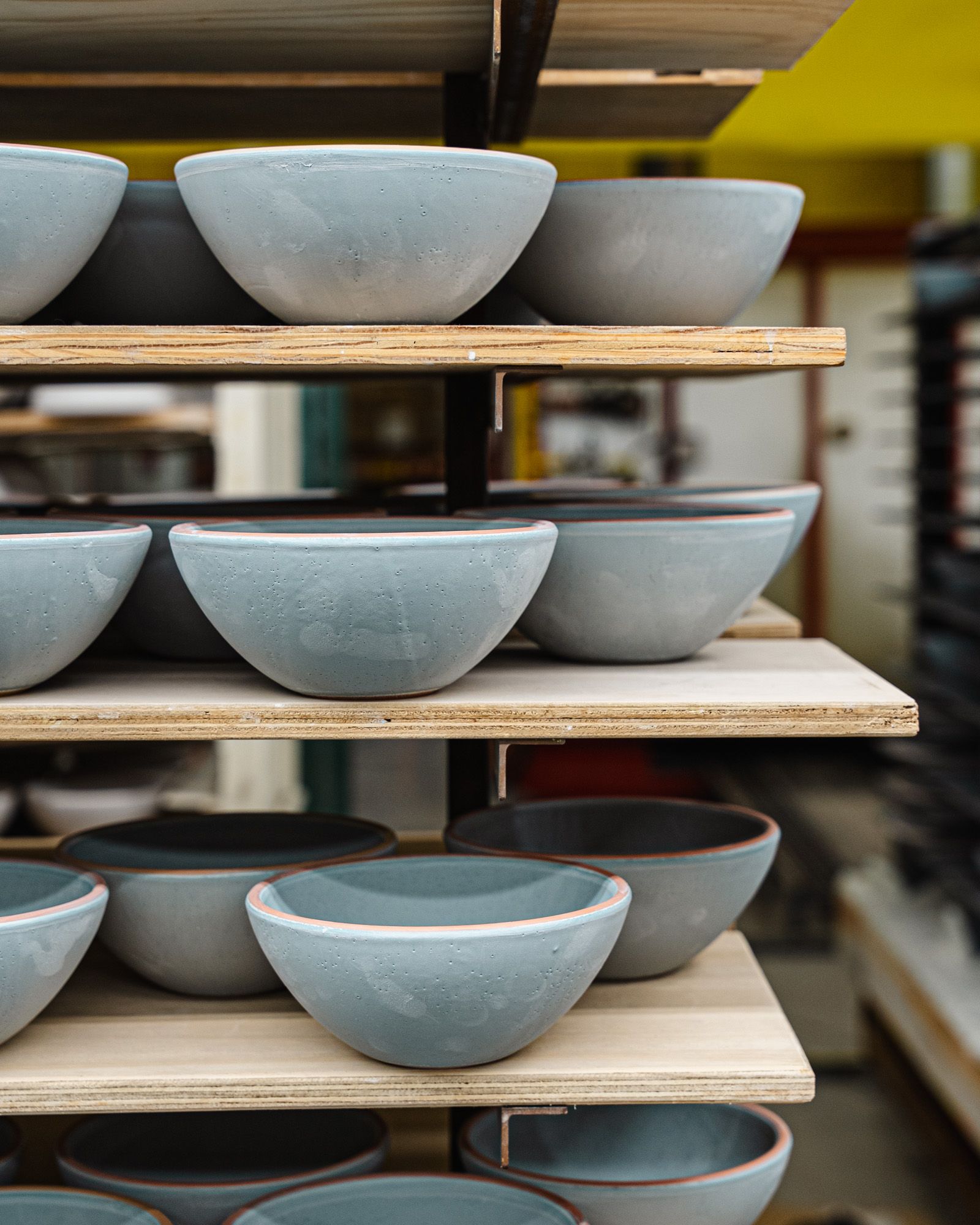 A shelf of glossy blue ceramic bowls waiting to be fired in the kiln.