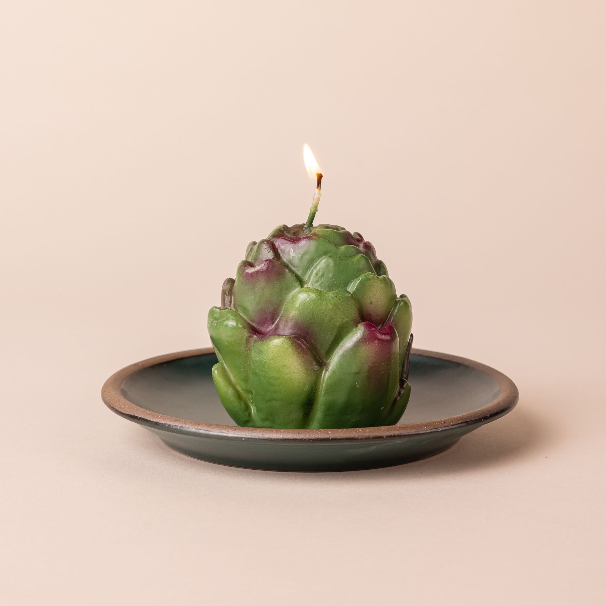 An artichoke candle with a burning flame sits on a small plate