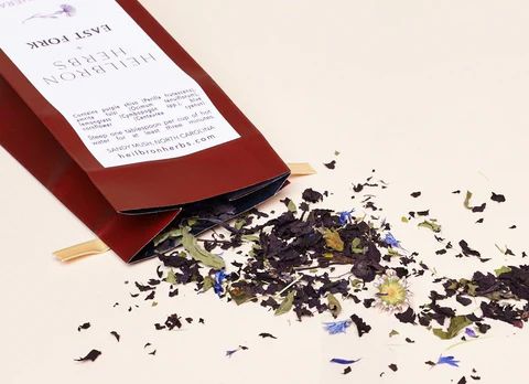 A package of Color Therapy tea is on its side spilling out the contents of dried tea on a table.