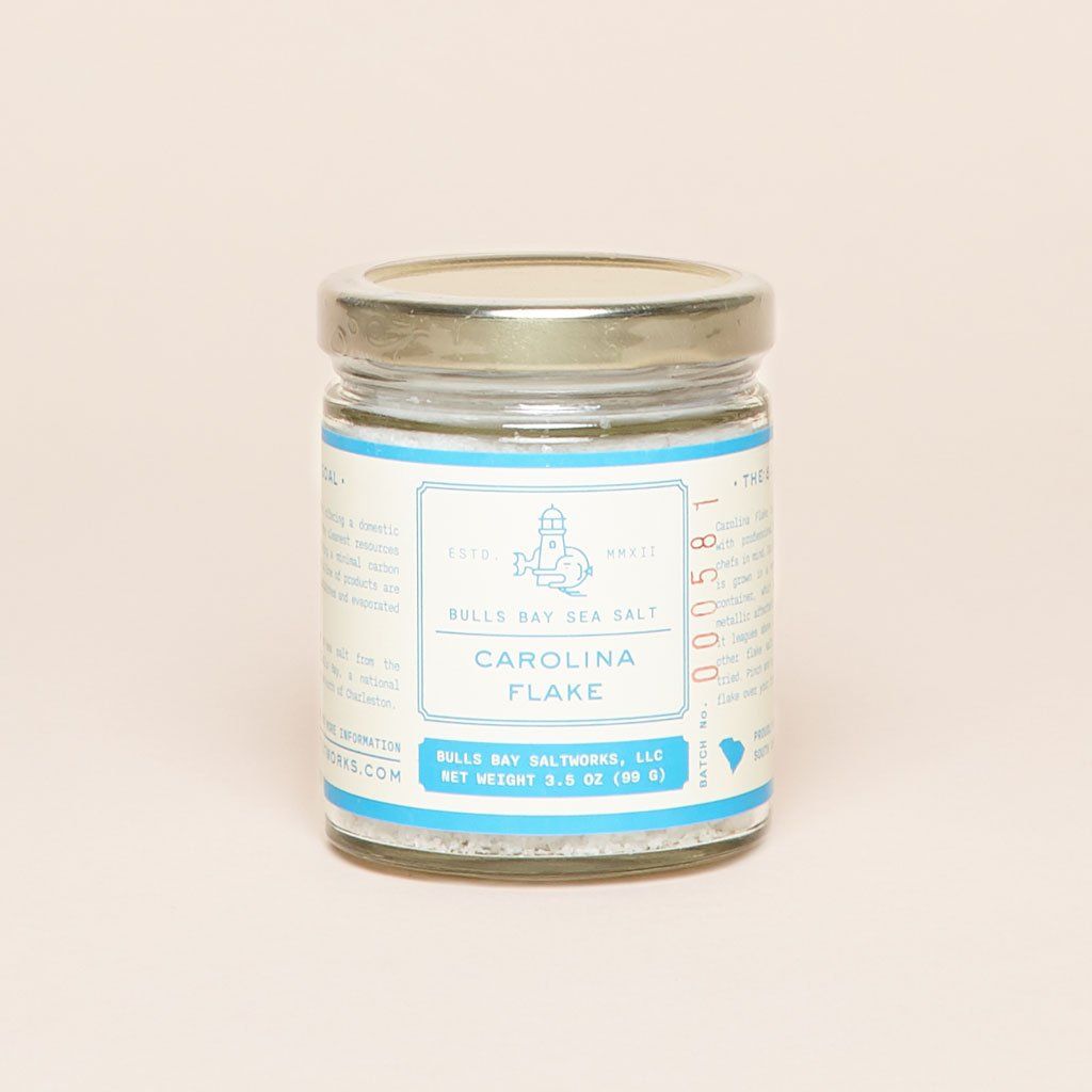 Carolina flake salt in a glass jar with gold lid and white and blue label 