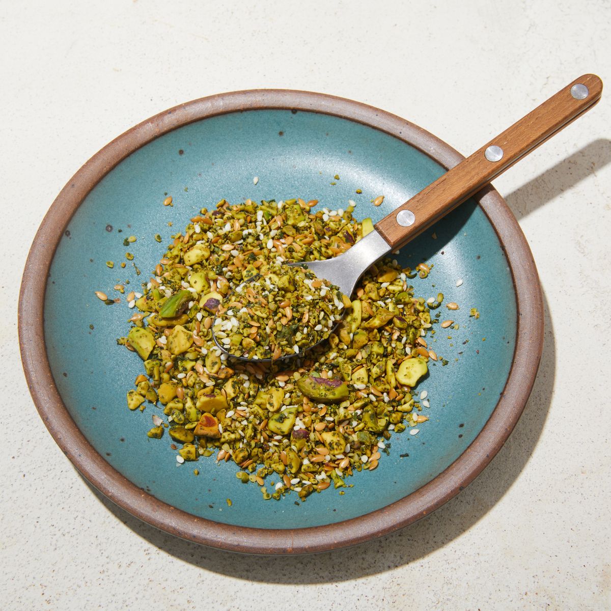Pistachio dukkah spread over a turquoise plate with spoon resting on top