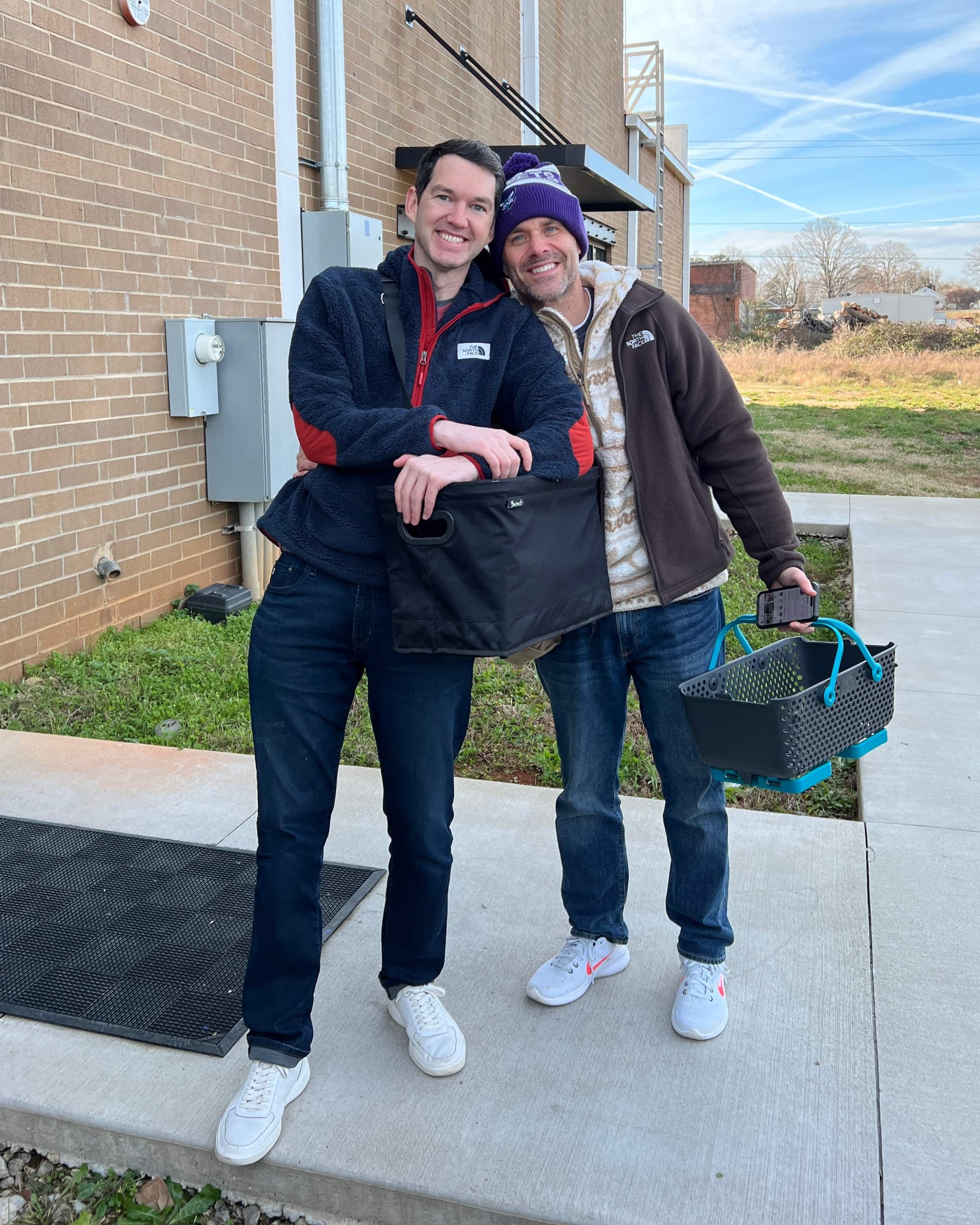 Chuck and Glen carrying baskets and smiling outside an East Fork Seconds Pop-up.