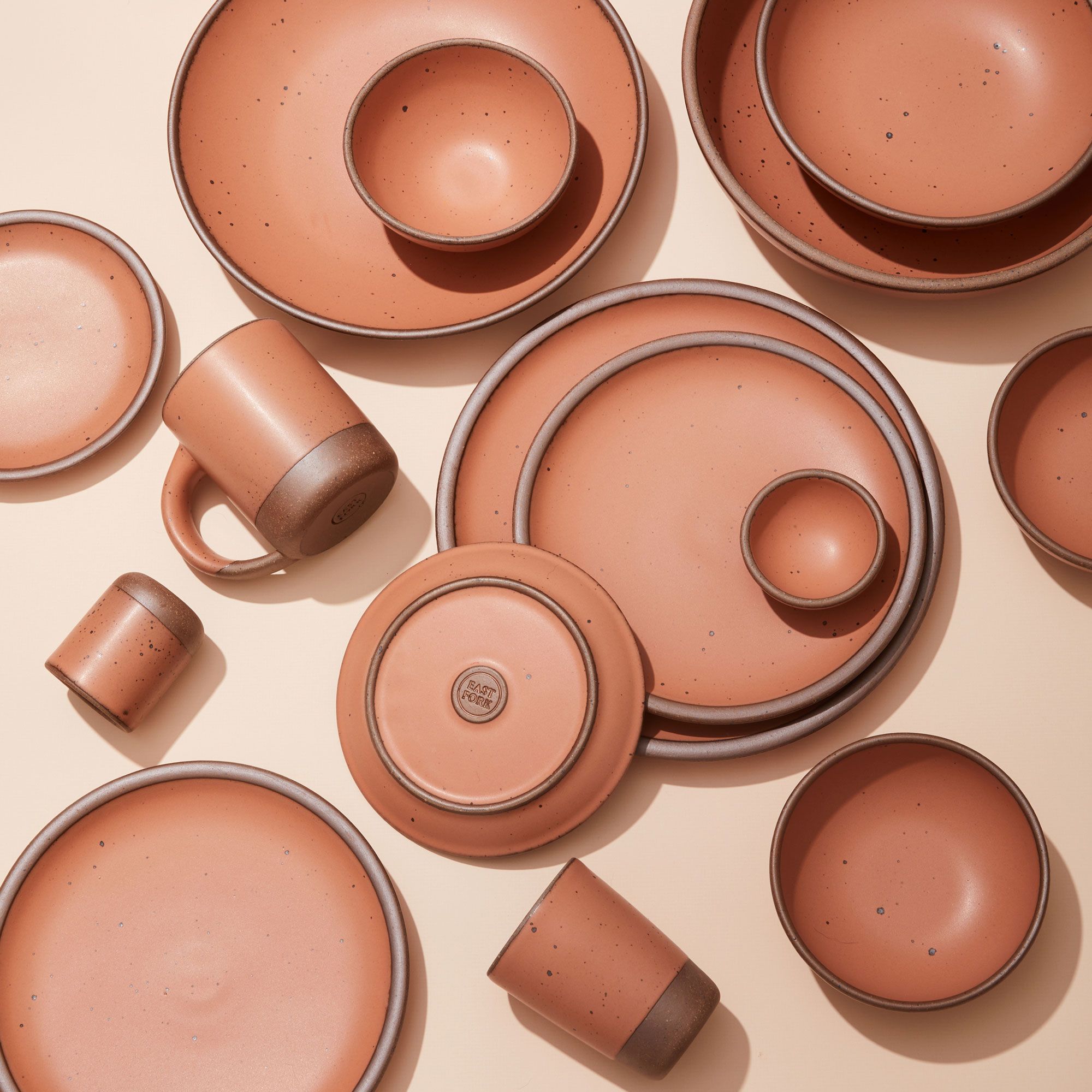 An overhead view of several plates, bowls, and cups, all in a warm peach color with unglazed rims.