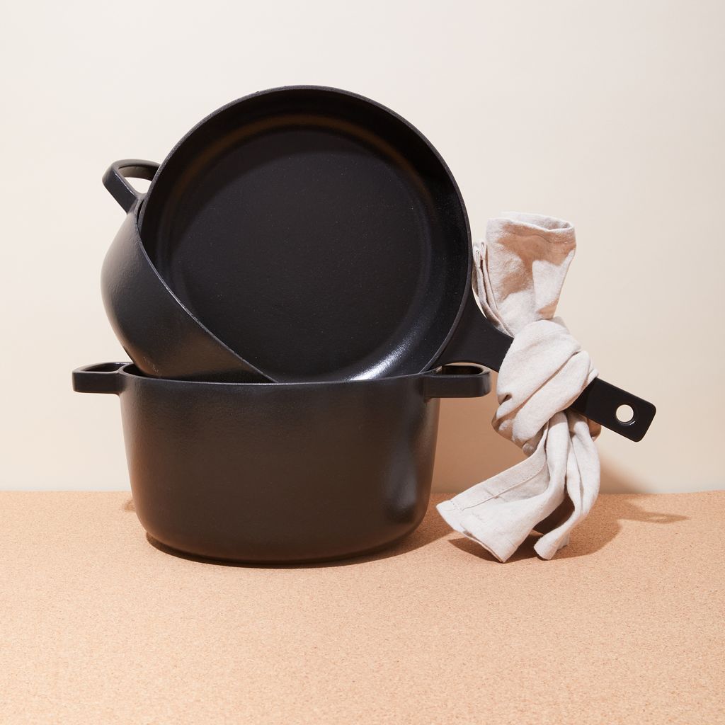 A stack of three black cast iron pots with a beige cloth tied around one of the handles