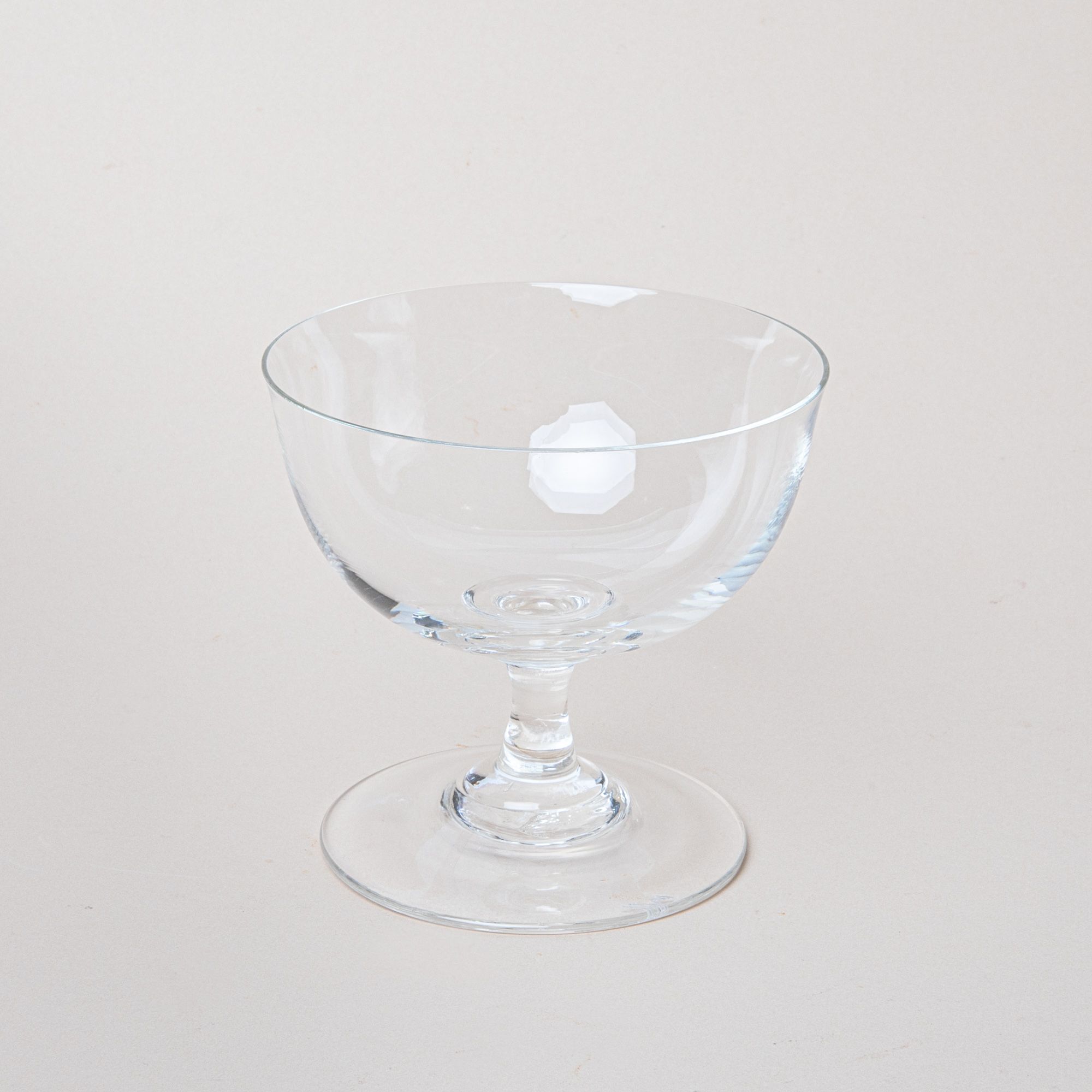 A clear coupe glass with a short stem and wide base