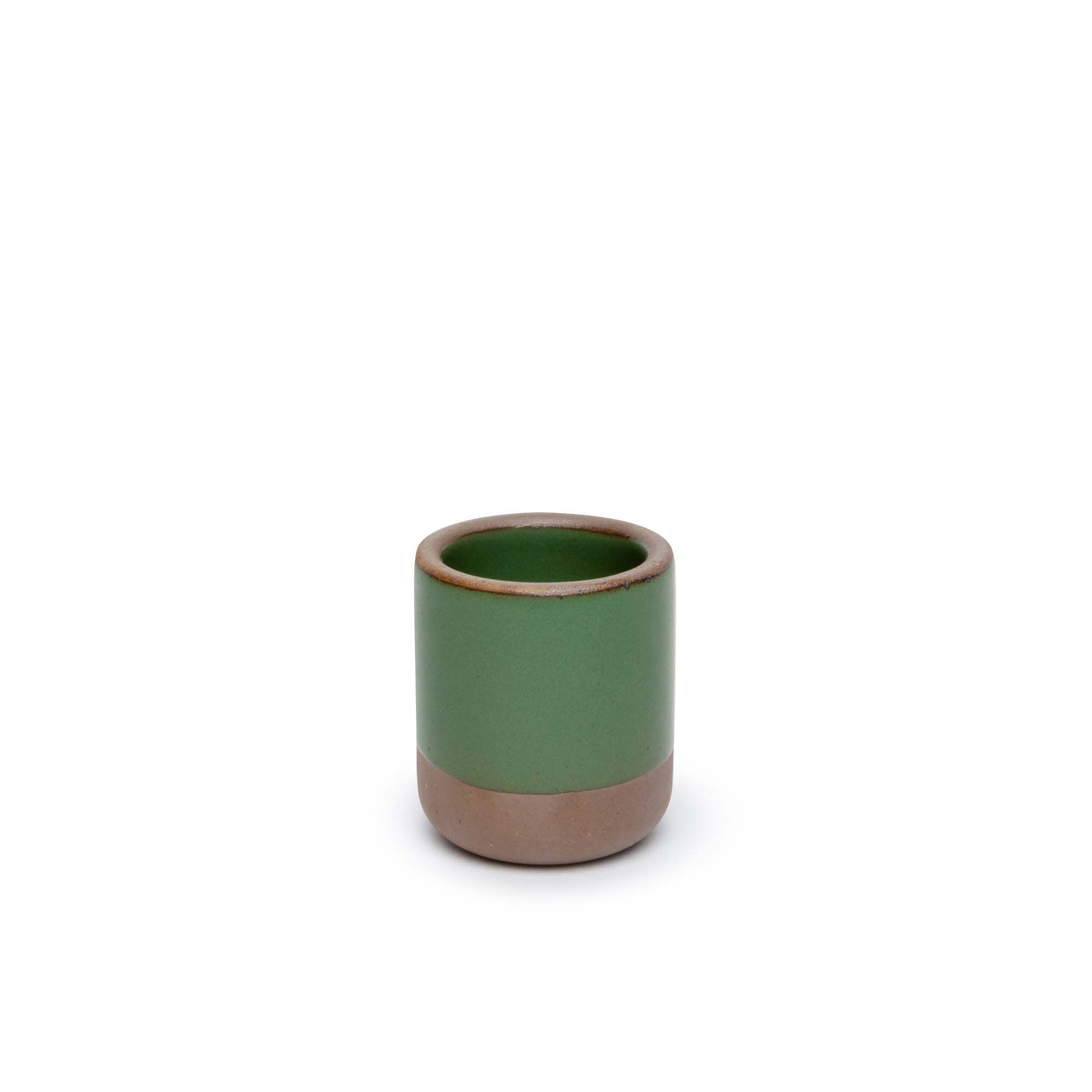 A small, short ceramic mug cup in a deep, verdant green color featuring iron speckles and unglazed rim and bottom base.
