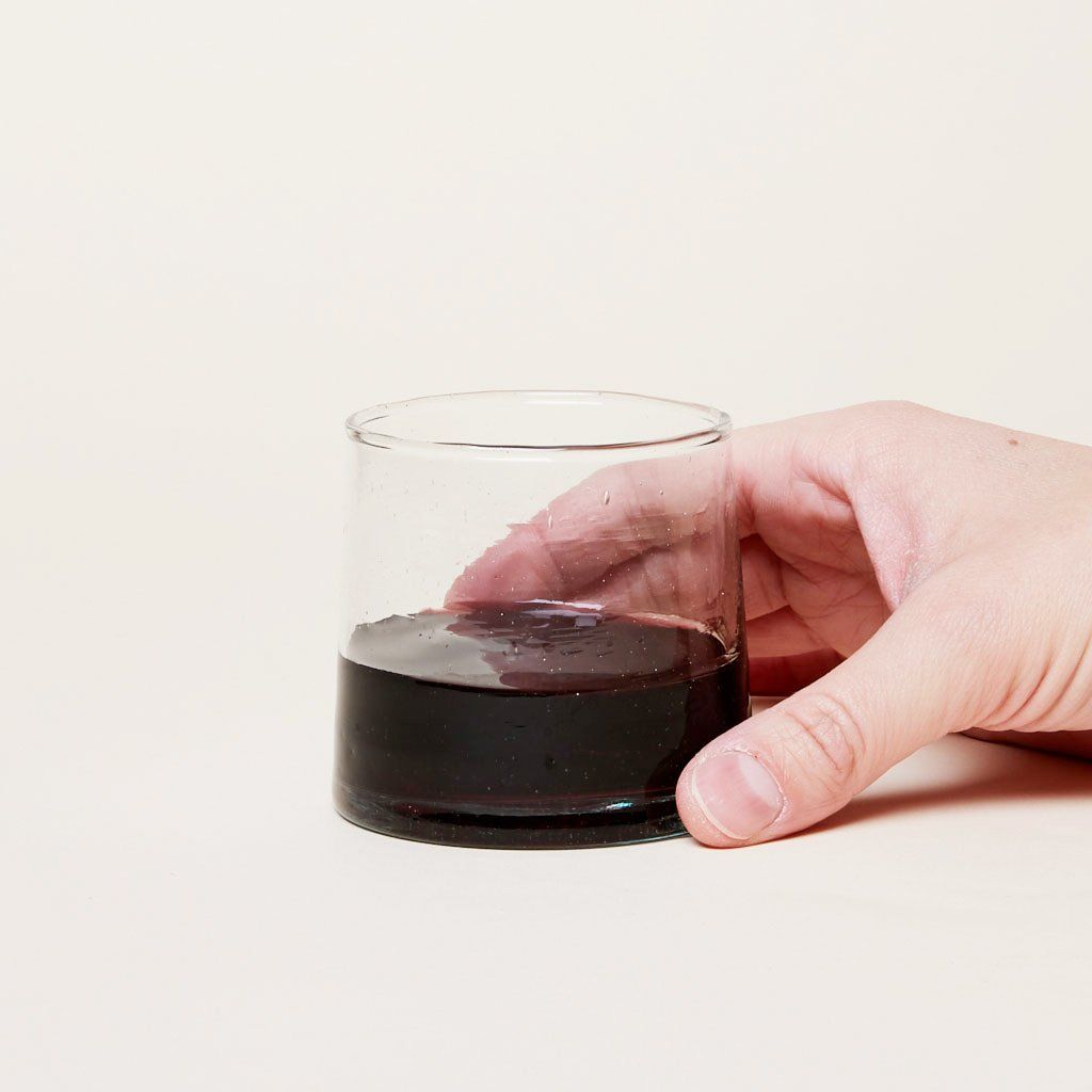 Hand holding a short recycled Moroccan glassware glass half-filled with red wine