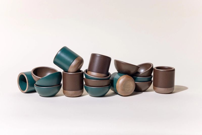 Small bowls and cups in ceramic dark teal and brown colors are haphazardly stacked in a row
