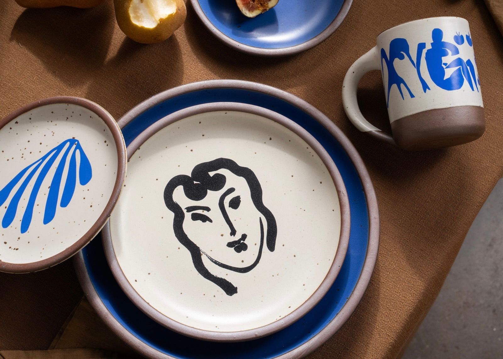 On a table are plates in a bright cobalt blue, with decorated plates and a mug featuring artwork by Henri Matisse.