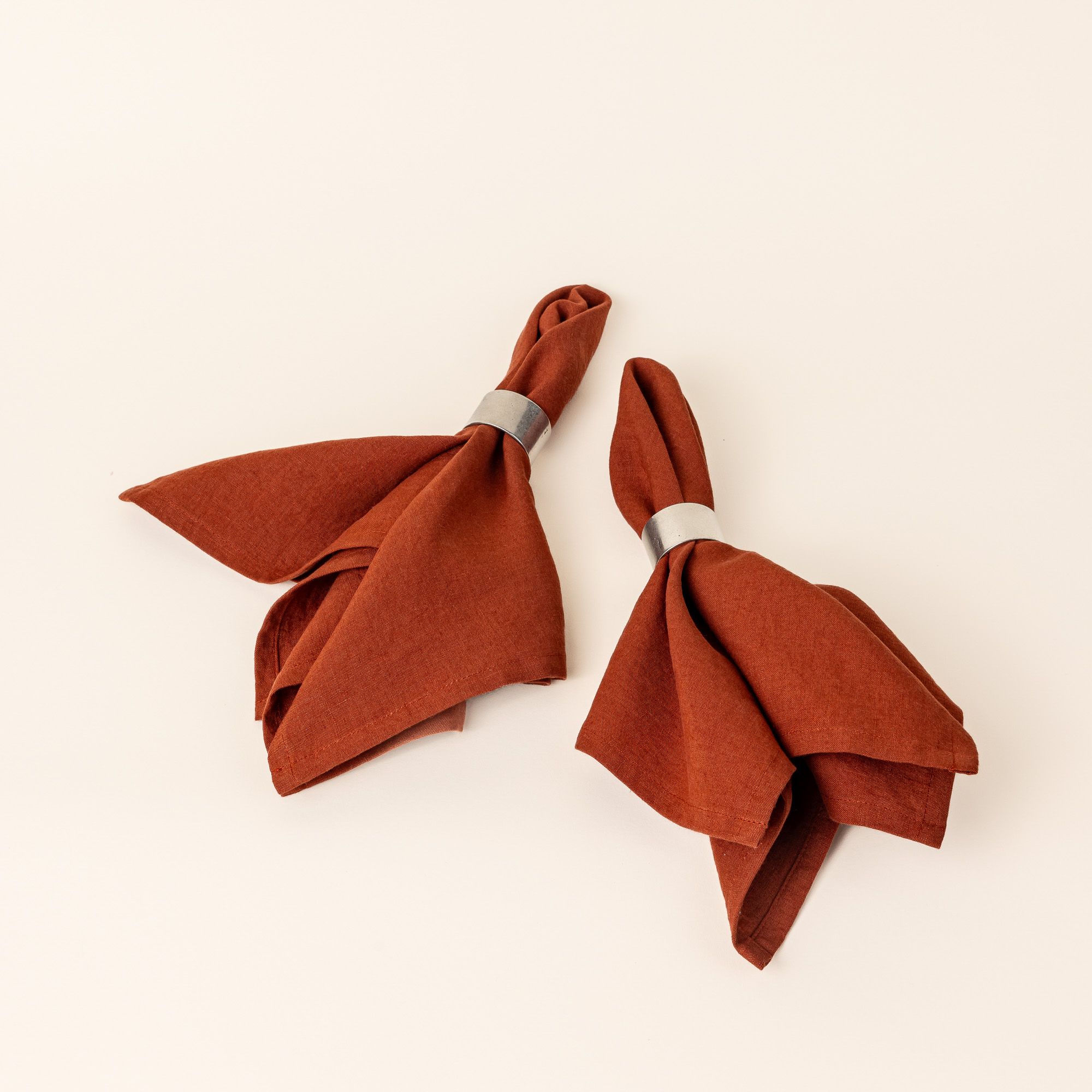 Two terracotta linen napkins are folded by the center through simple pewter napkin rings.