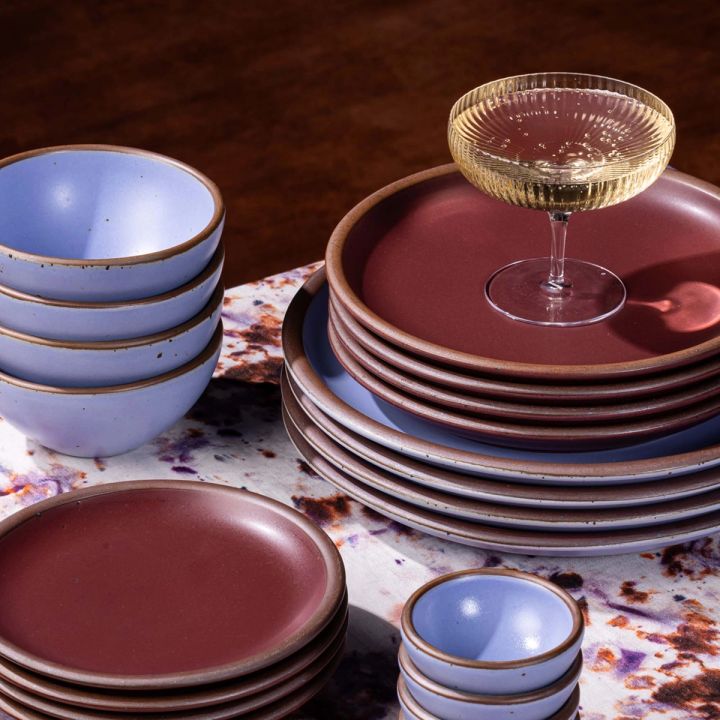 A ribbed traditional coupe glass filled with champagne sitting on a stack of ceramic plates in periwinkle and plum colors