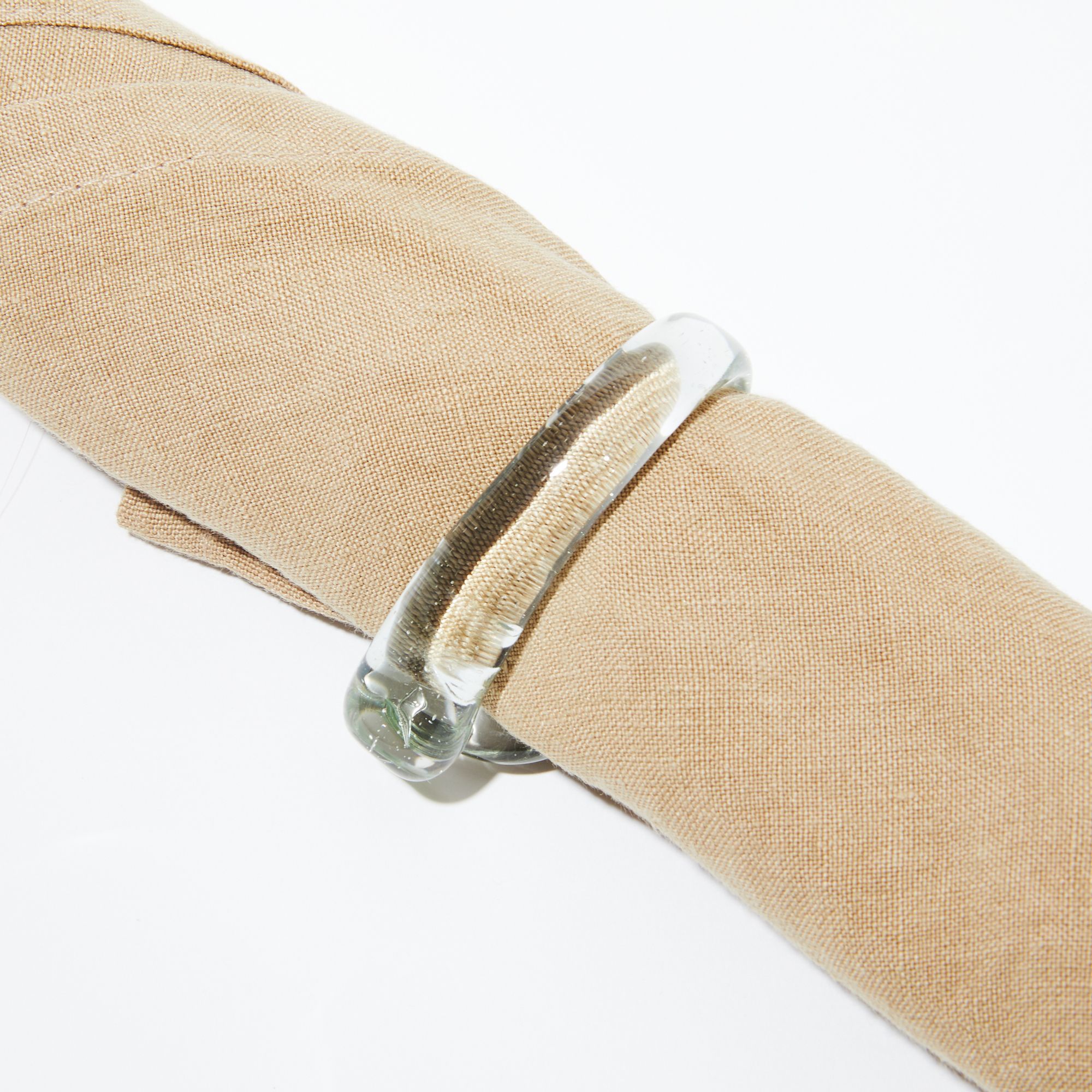 A glass napkin ring wrapped around a natural beige linen napkin