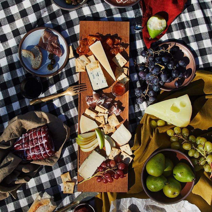 Charcuterie board with assortment of real and faux meats, cheeses, and fruits on a gingham blanket. A true picnic feast.