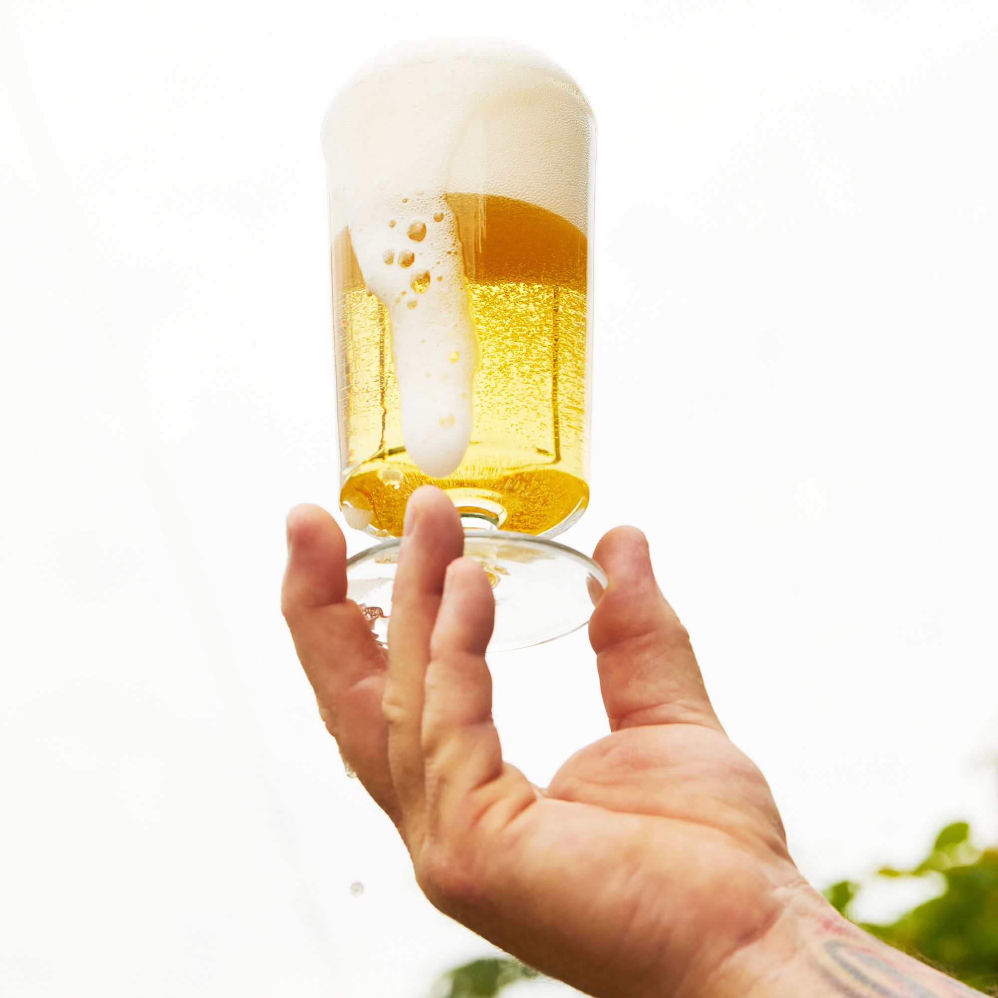 hand holding long bodied footed glass filled with beer, foaming at the top