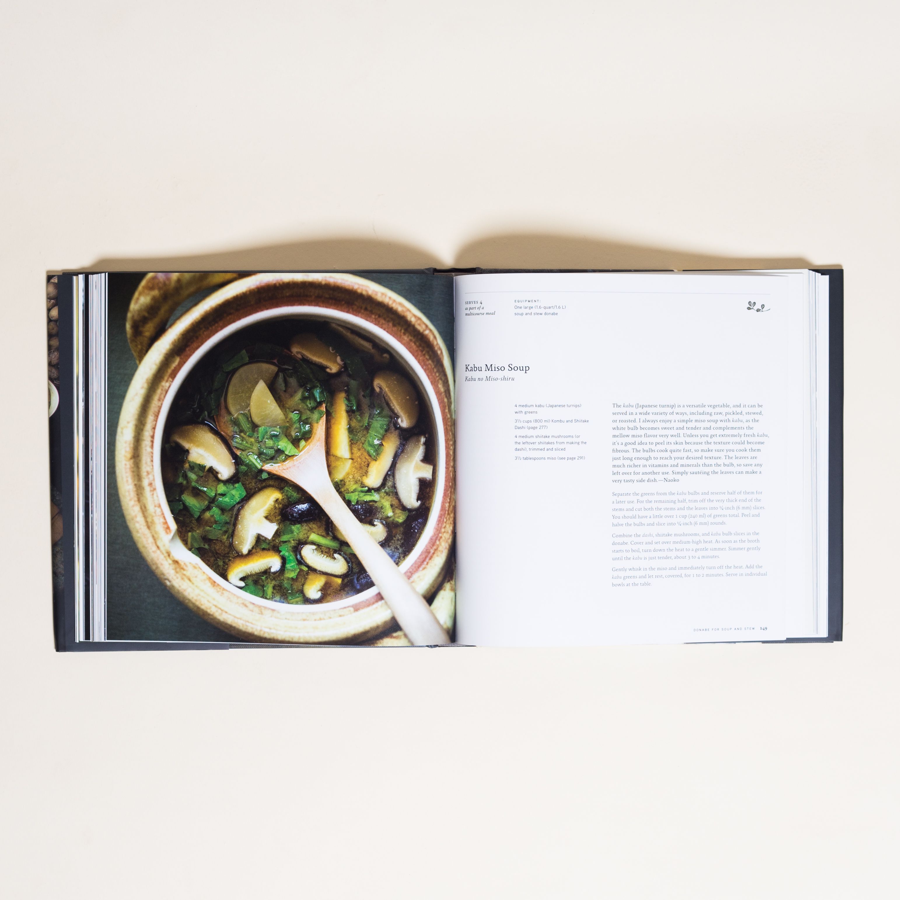 A two-page spread in a cookbook showing a pot with liquid, mushrooms and green vegetables with a wooden spoon and the recipe for the soup