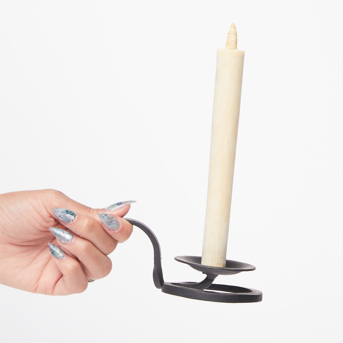 Hand holding a black cast iron candle holder with a circular base containing a tall cream candle