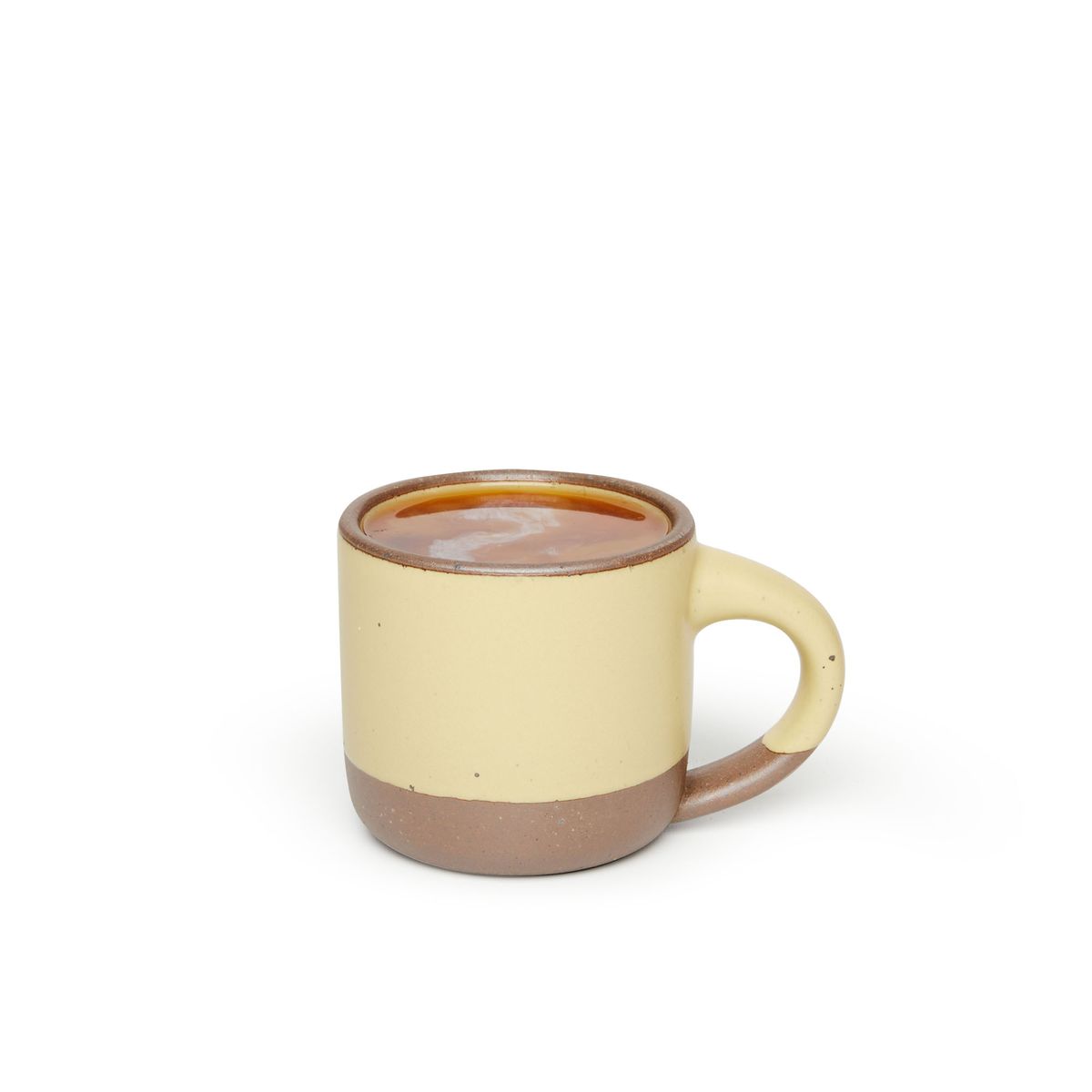 A small sized ceramic mug with handle in a light butter yellow glaze featuring iron speckles and unglazed rim and bottom base, filled with coffee.