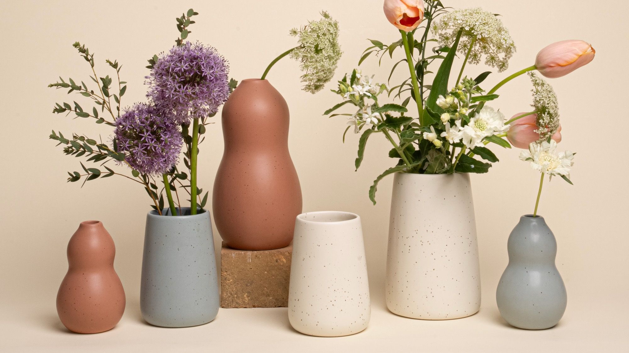 Ceramic vases in curvey and sloped forms in cream, warm terracotta, and soft pale blue with flowers.