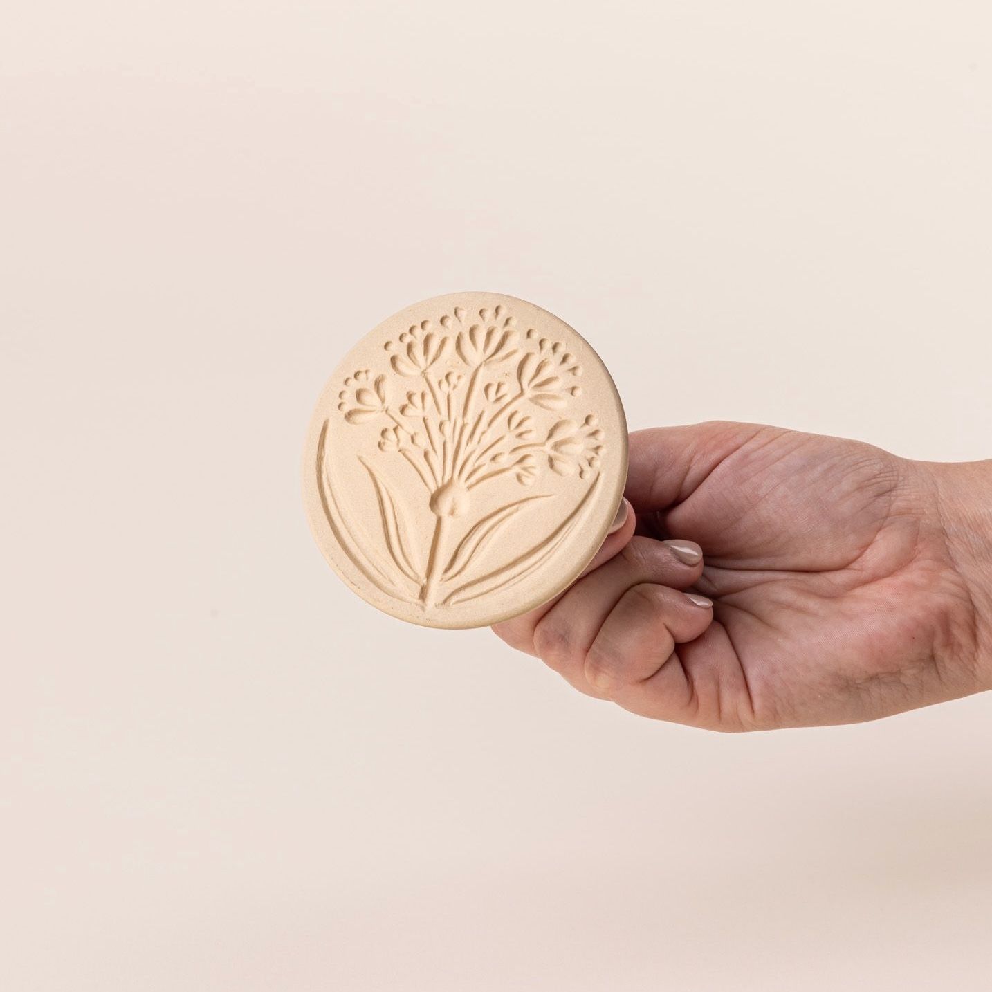 Hand holding a cookie stamp showing the bottom featuring the design of an allium