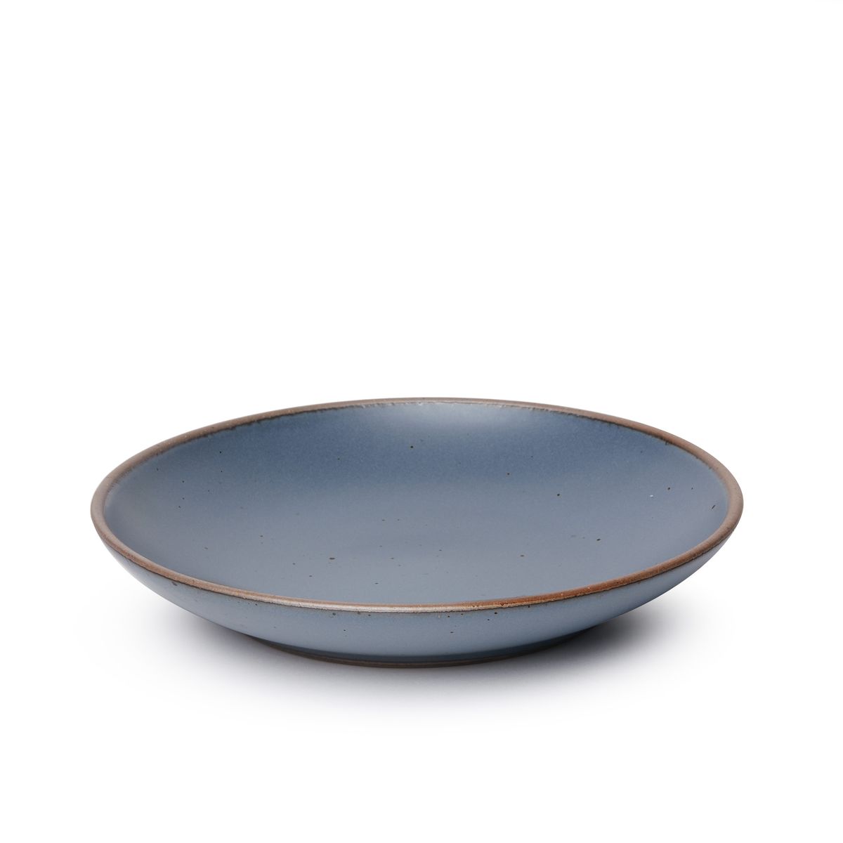 A large ceramic plate with a curved bowl edge in a cool, medium blue color featuring iron speckles and an unglazed rim.