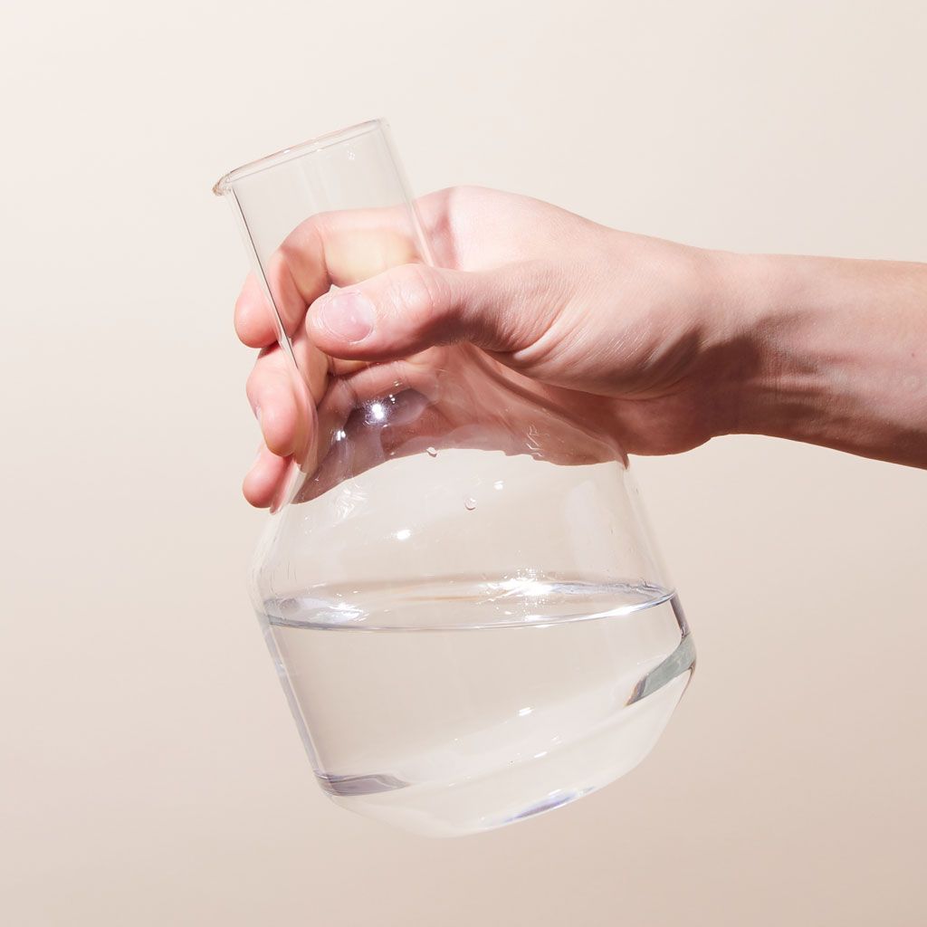 Hand holding a clear glass carafe with a large base and thinner neck