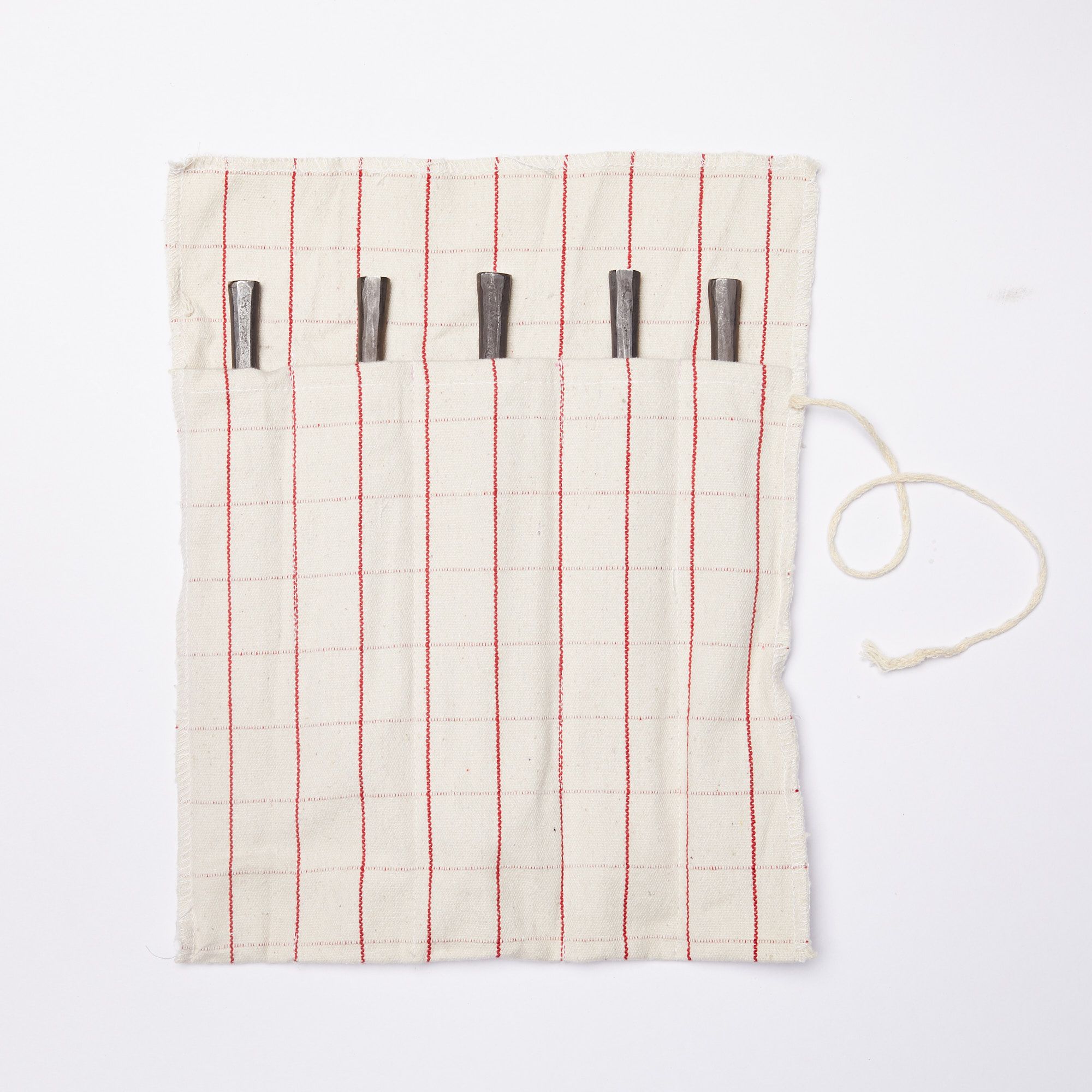 Utensil roll, made of cream color fabric with a thin red grid pattern, unfurled with the end of five utensil handles peeking out of their pockets