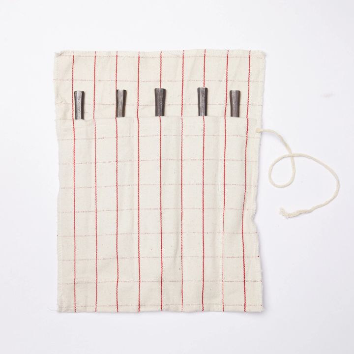 Utensil roll, made of cream color fabric with a thin red grid pattern, unfurled with the end of five utensil handles peeking out of their pockets